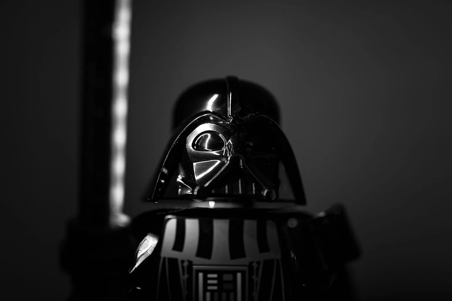 Black-and-white portrait of a LEGO Darth Vader figure with a glowing lightsaber in the background