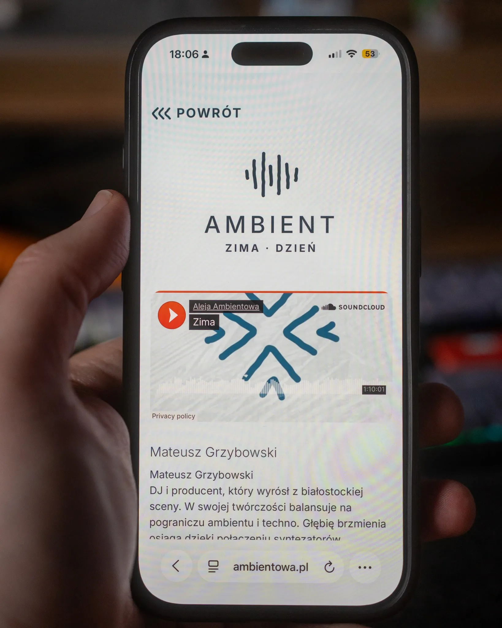 A phone showing ambientowa.pl in its Winter – Day variant, playing a set by Mateusz Grzybowski