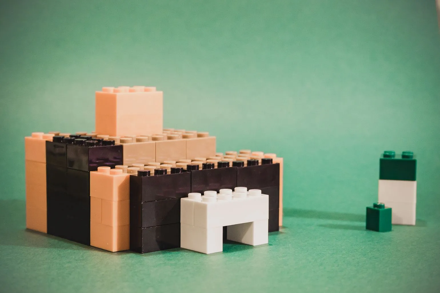 Low building of beige and dark brown LEGO bricks with a white entrance arch, on a green background