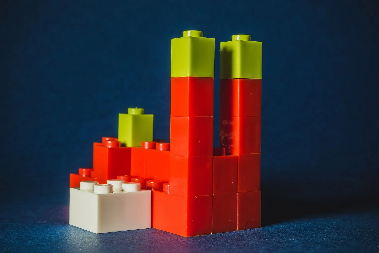 Two red LEGO towers with green tops and a lower section with a white brick, against a navy background