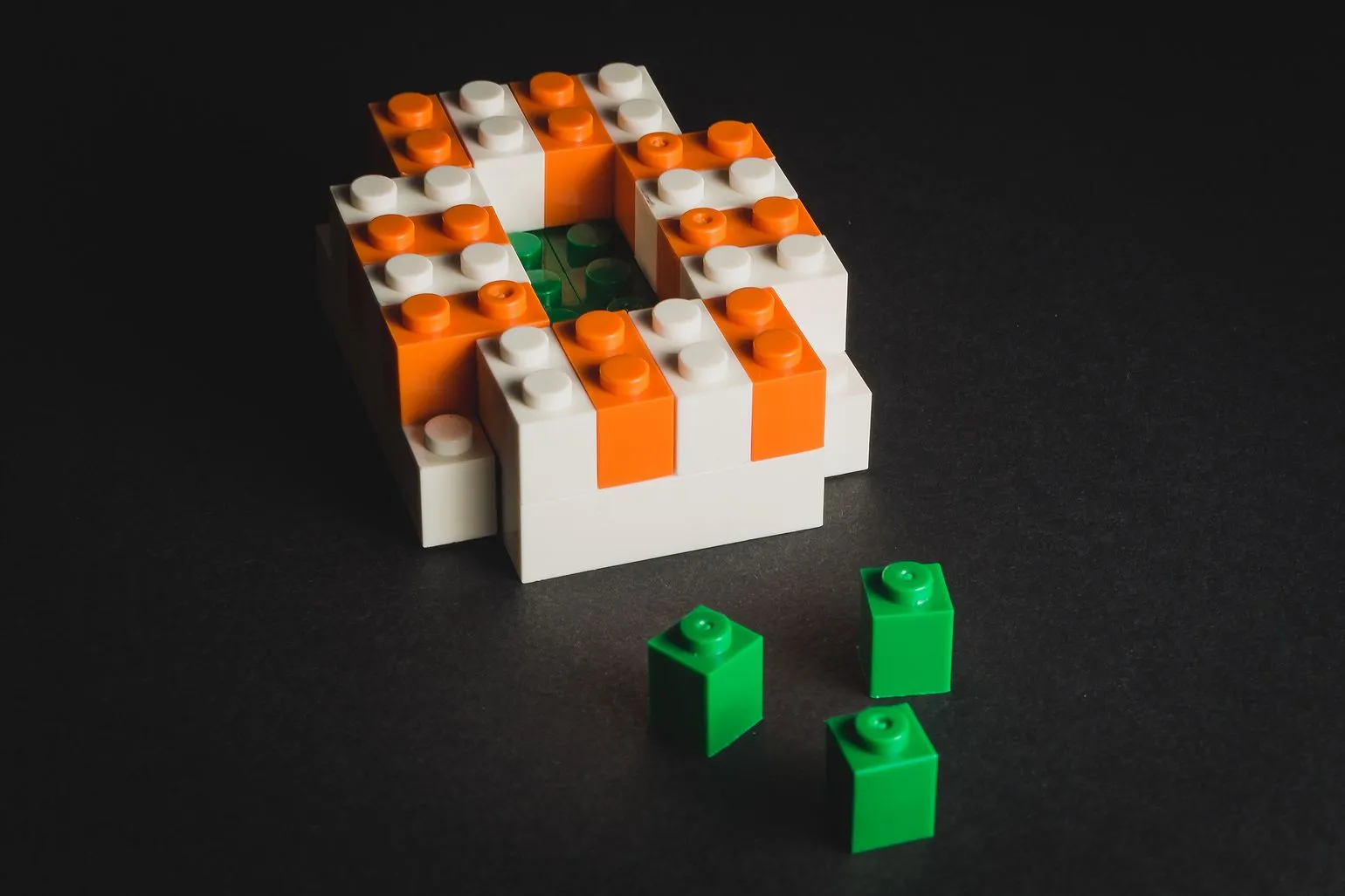 Oval structure of orange and white LEGO bricks with a green centre, three green bricks beside it