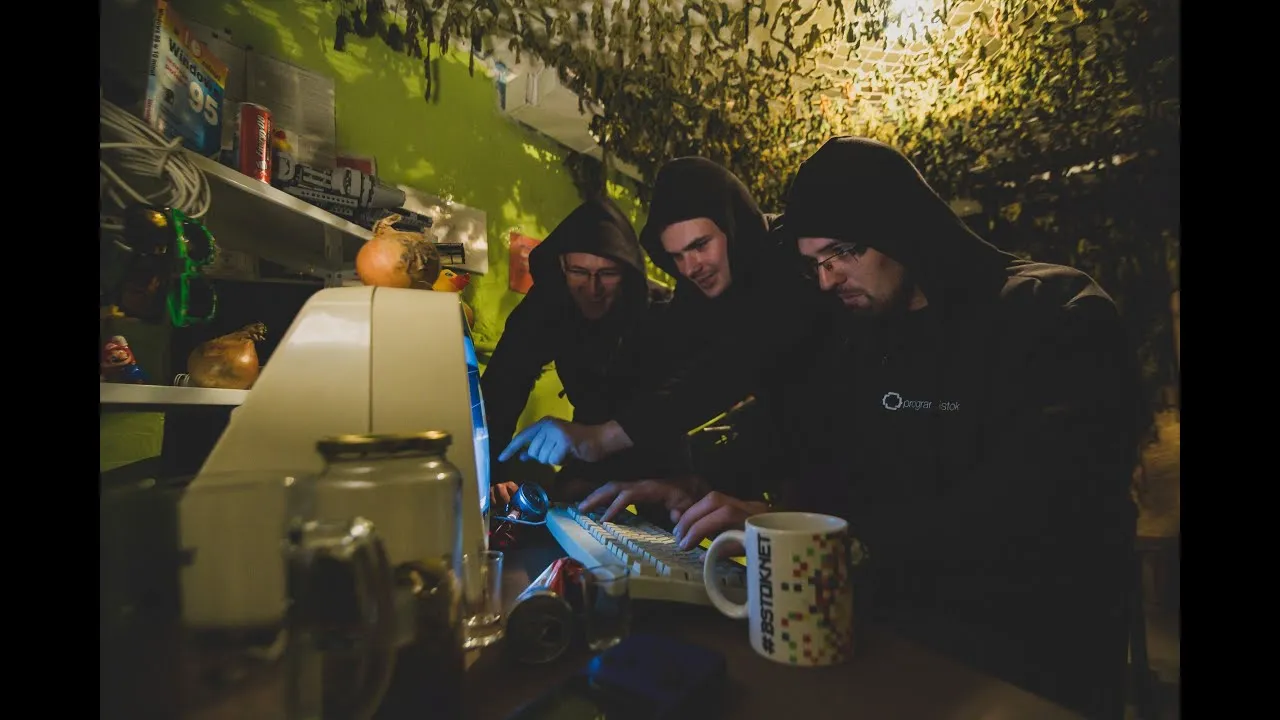 Three hooded men hunched over an old computer in a dark, cluttered basement – a still from the Programistok 2016 music video