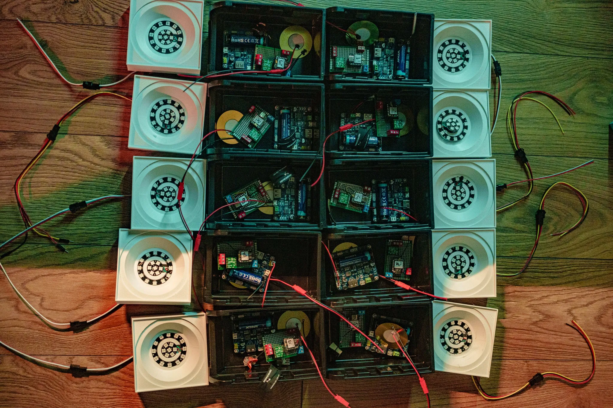 Ten electronics boxes and ten 3D-printed panels with LED rings laid out on a wooden floor