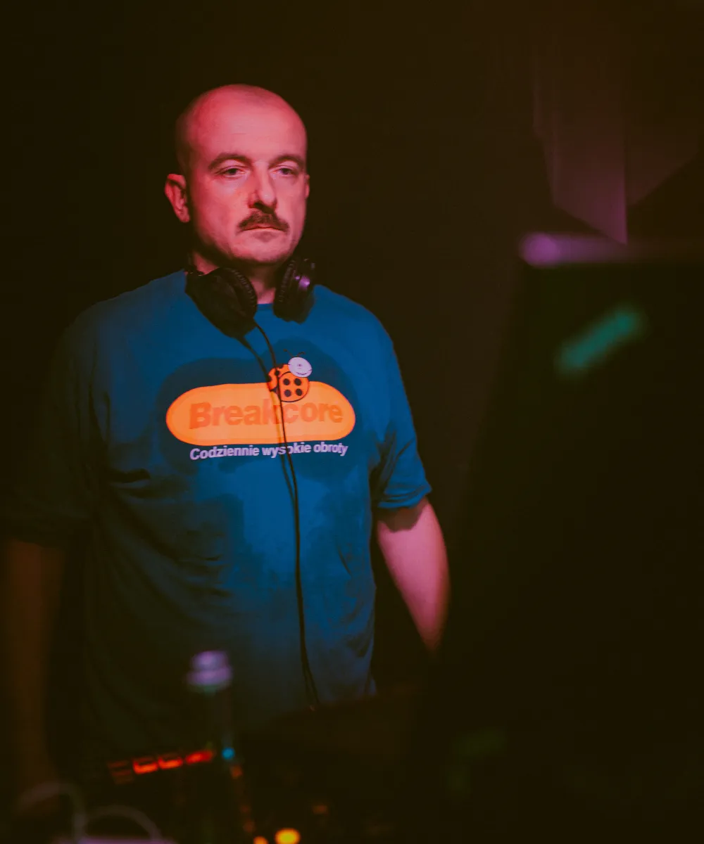 A DJ with headphones round his neck, in a blue T-shirt, in a dark club
