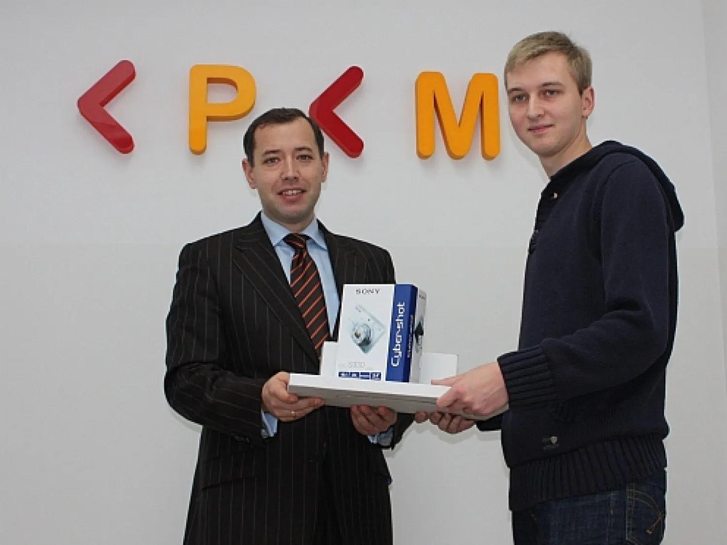 KPKM vice-president Marcin Moskwa handing Maciej Korsan a digital camera in front of the KPKM logo