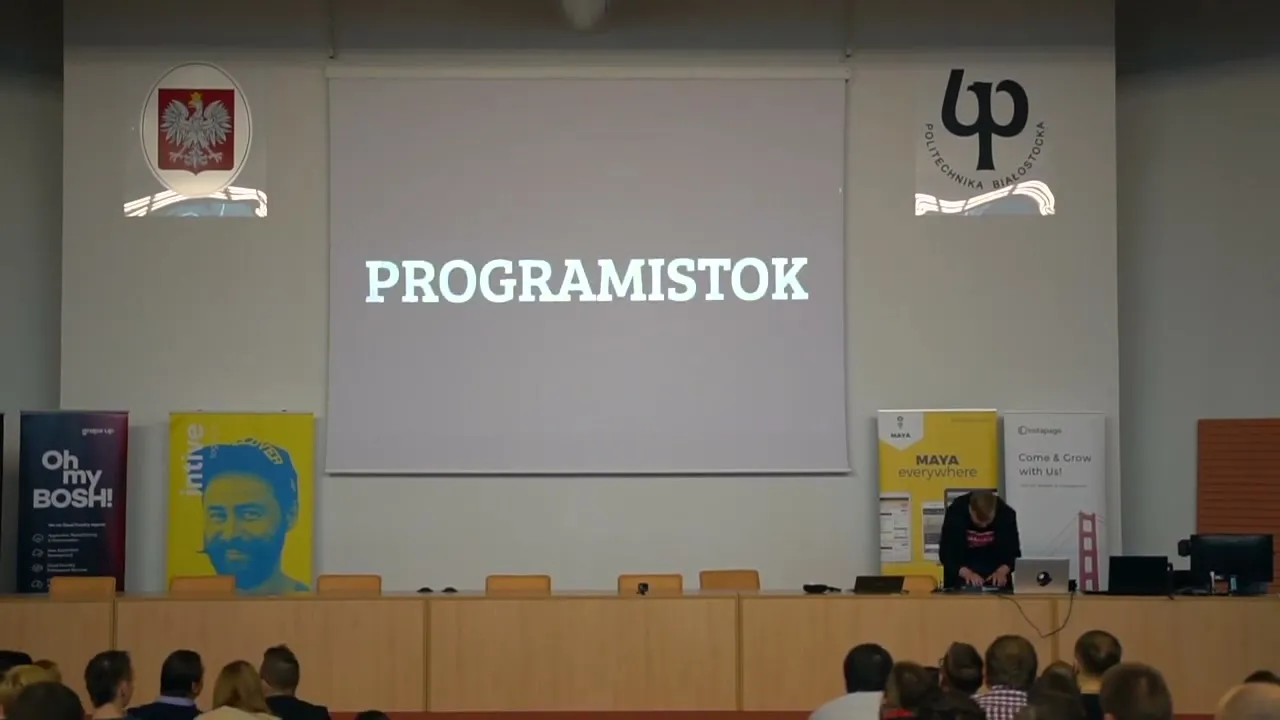 Lecture hall with the Polish emblem and the Białystok University of Technology logo; PROGRAMISTOK on the screen, a person at a laptop below it, the audience in the foreground