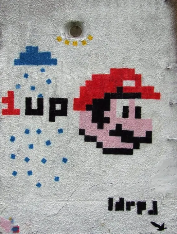 A pixelated Mario head in a red cap painted on a white wall, next to the word “1up” and a blue cloud dripping pixel raindrops