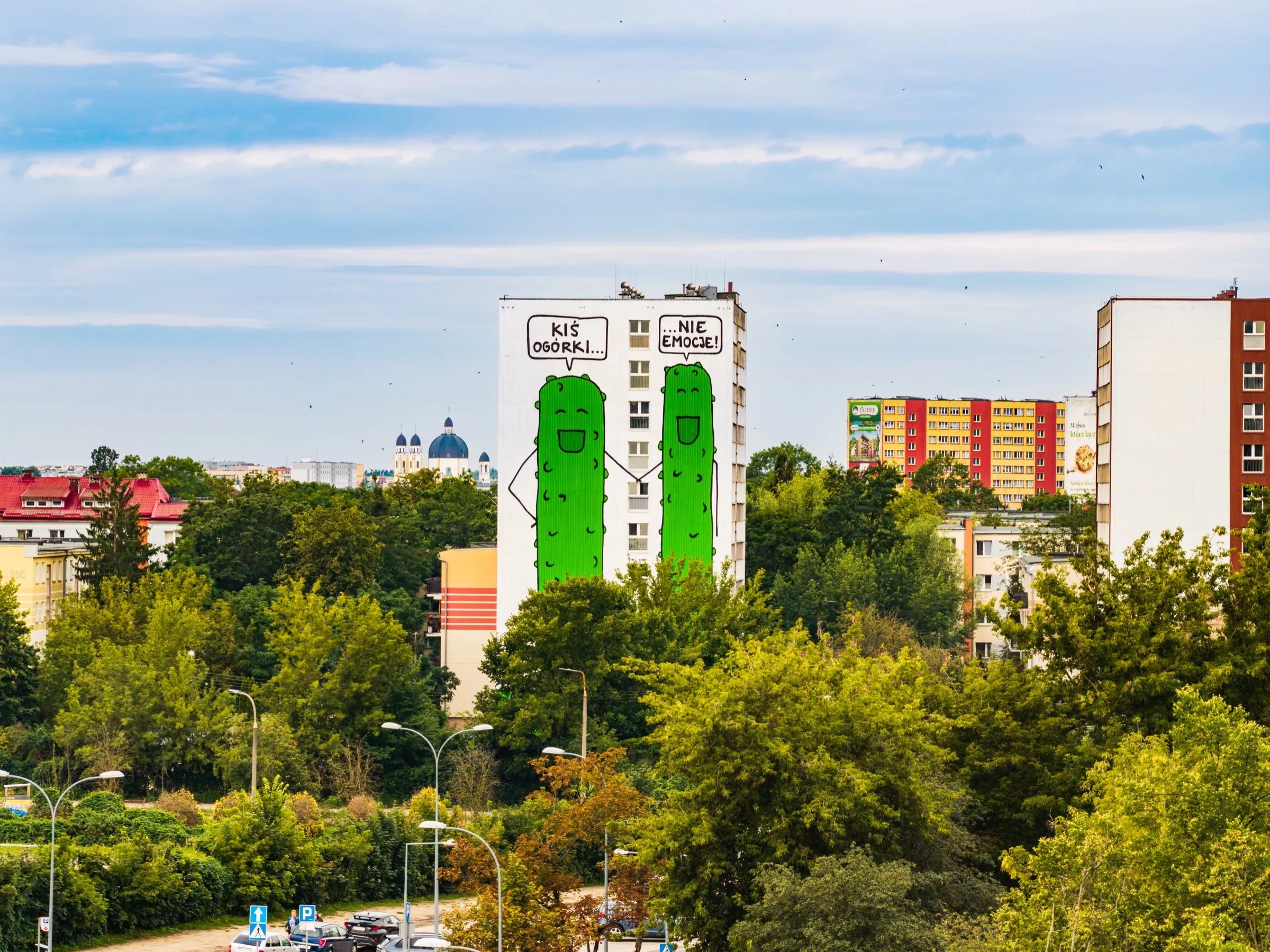 The two-cucumber mural on the dorm rising above green treetops, with Orthodox church domes and colourful apartment blocks in the background