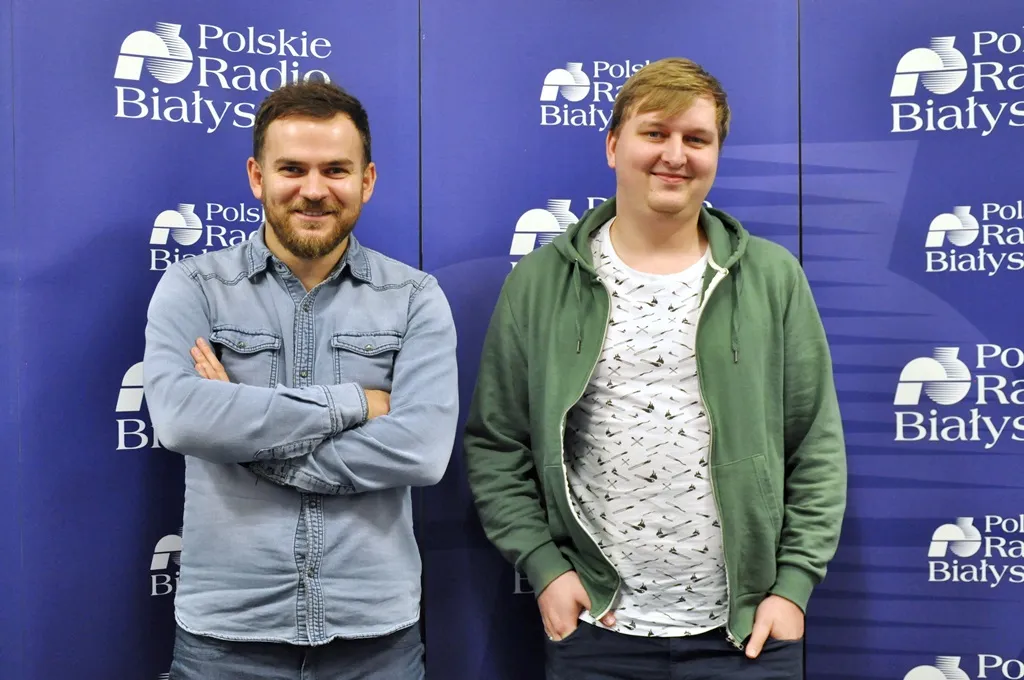 Two men posing in front of a Polskie Radio Białystok logo wall