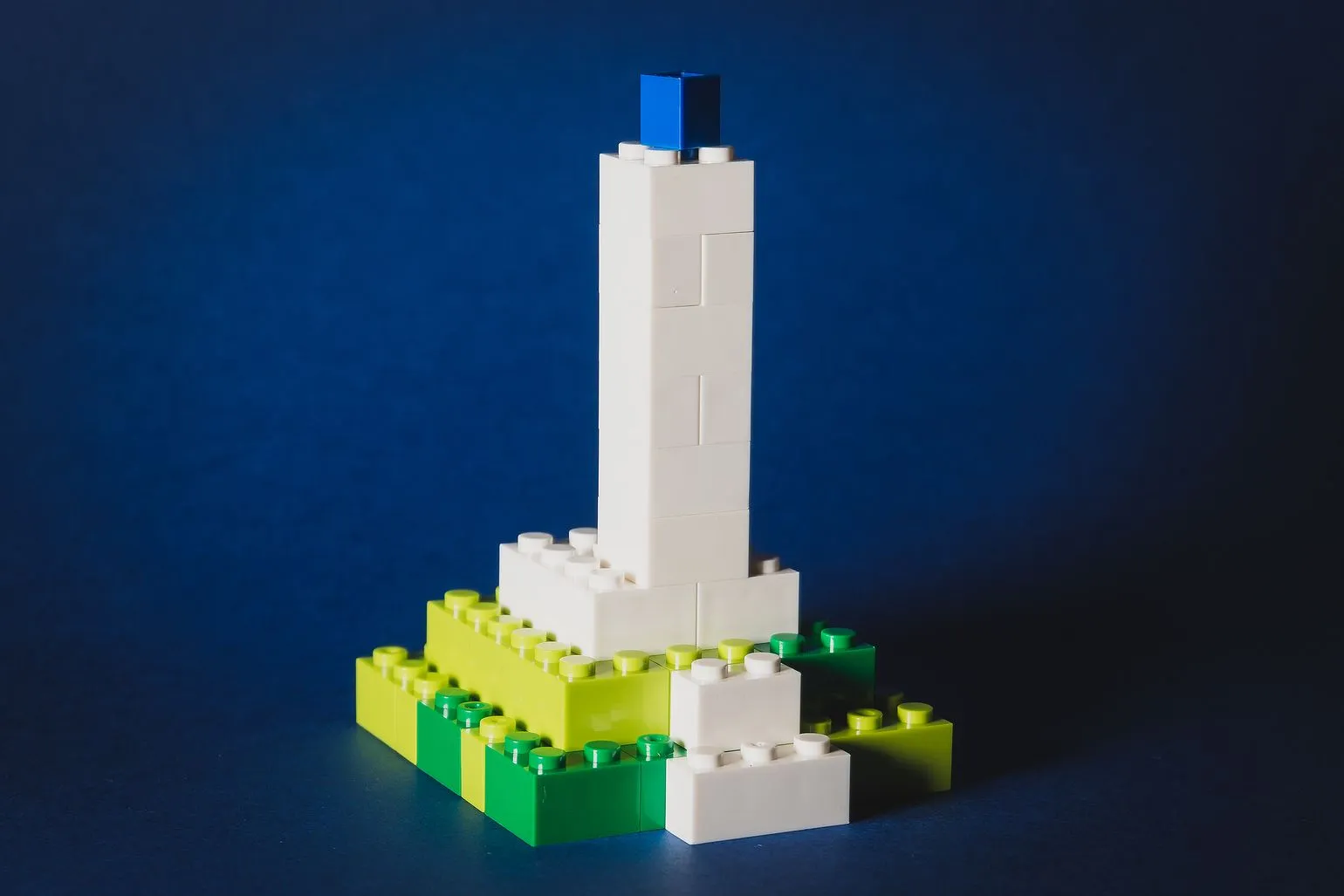 Tall white LEGO tower topped with a blue brick, on a green and yellow base, against a navy background