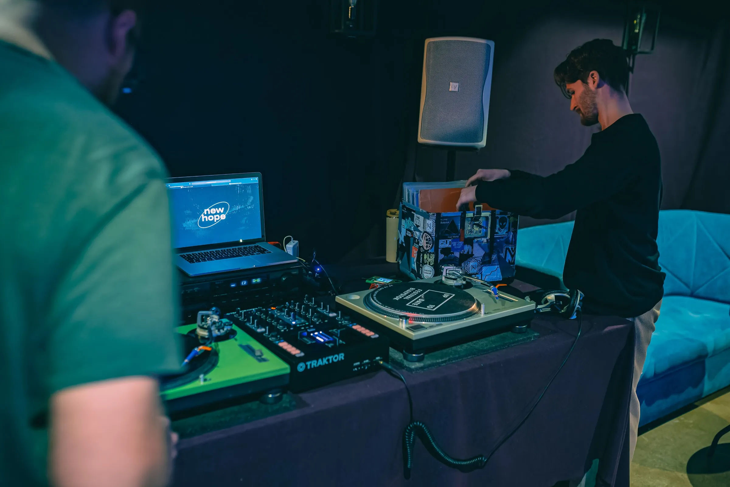 Projekt New Hope DJ school: a young man pulls a record from a crate, with turntables, a Traktor mixer and a laptop showing the New Hope logo in front of him