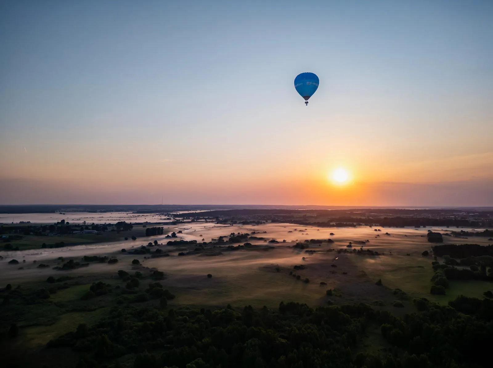 Blue hot-air balloon over misty meadows at sunrise
