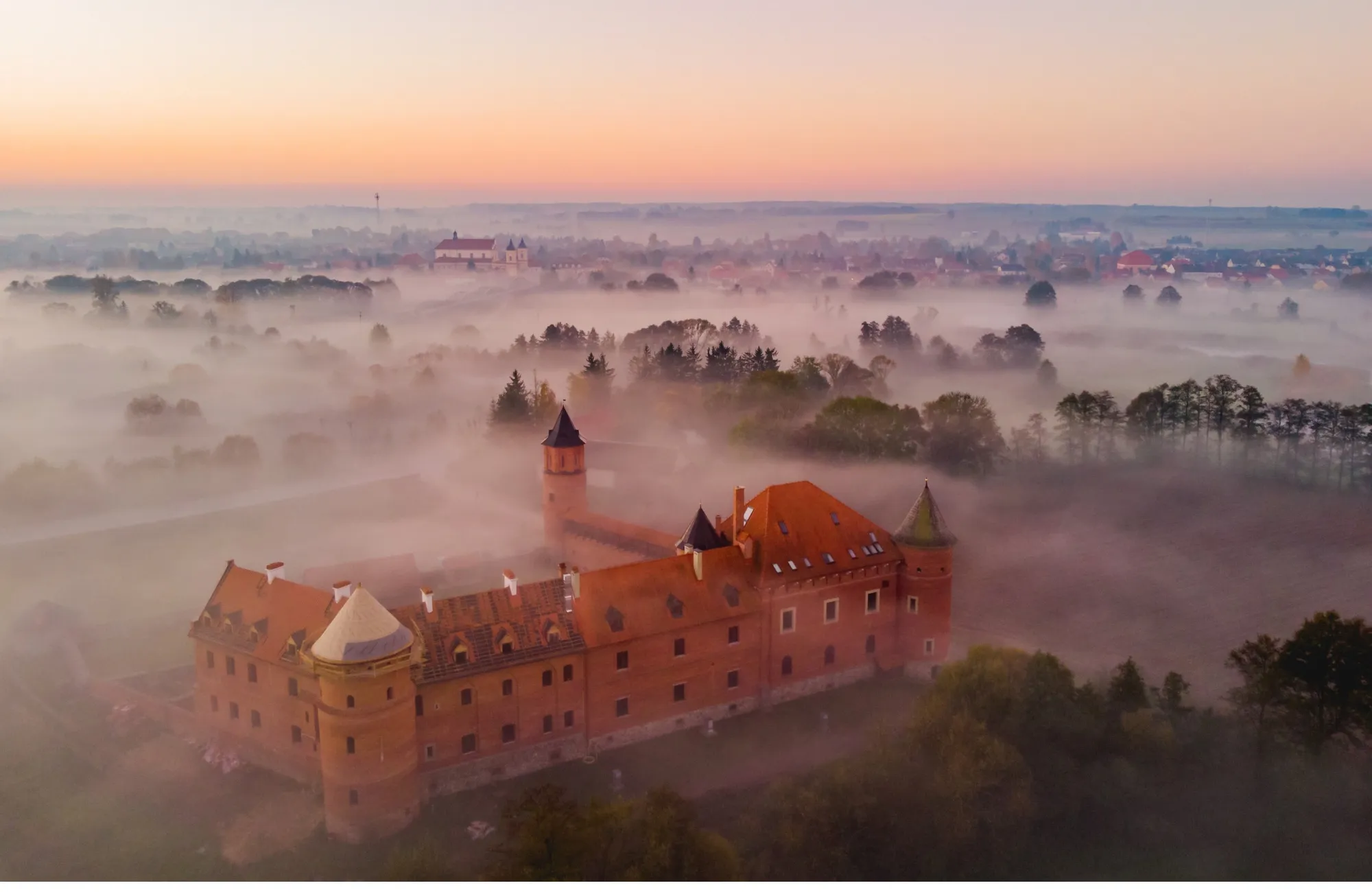 Aerial view of Tykocin Castle above the morning fog, with the town and its church behind
