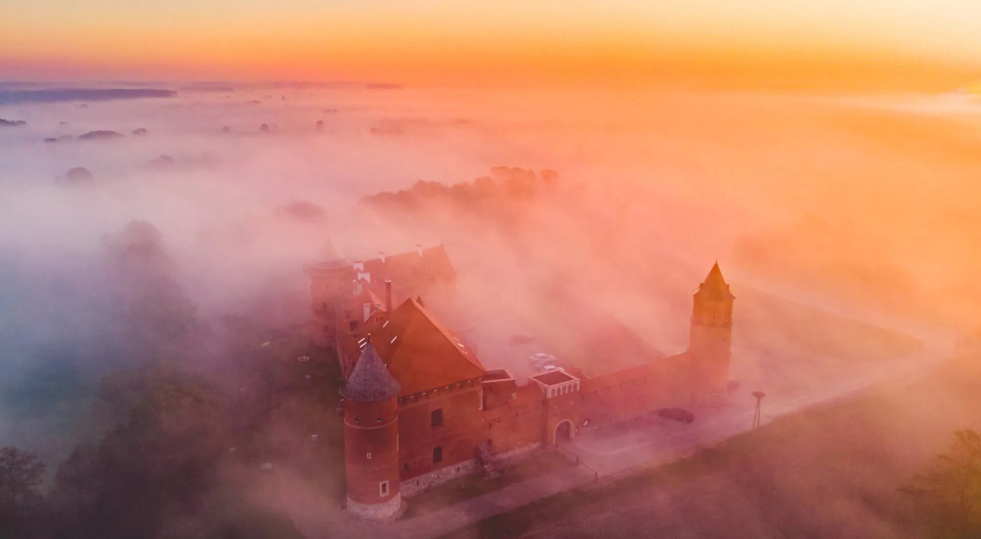 Aerial view of Tykocin Castle wrapped in pink morning mist at sunrise